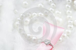 Diamond ring and pink ribbon on pearl necklace background