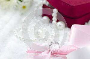 Diamond ring and pink ribbon on pearl necklace background