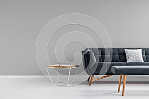 Diamond shape side table, a trendy, dark sofa and an upholstered bench in a gray living room interior with copy space. Real photo.