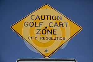 A diamond shaped traffic sign stating Caution Golf Cart Zone Ahead