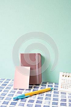 Diary note, pen, and calendar on blue tile desk. mint wall background. workspace