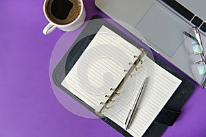 Diary, pen, laptop, glasses, a Cup of black coffee on a purple background