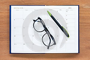 Diary planner book open july calendar page with glasses and pen on th