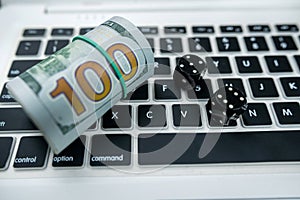 Dice and dollar bills on a new laptop keyboard isolated on a black table.