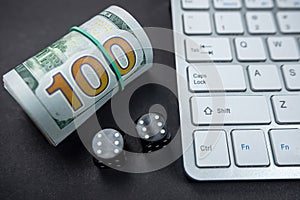 Dice and dollar bills on a new laptop keyboard isolated on a black table.