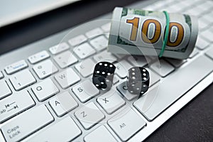 Dice and dollar bills on a new laptop keyboard isolated on a black table.