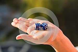 Dice 4 4 in the female hand, sunset background. Gambling devices.