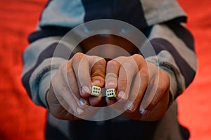 Dice in the hands of a man in a hood on a red background.