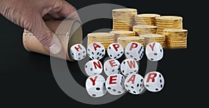 Dice spelling Happy New Year when tumbling out of a raffle cup hold by one hand with stacks of golden coins on black background.