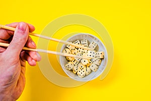 Dice in white bowl with chopsticks on yellow background
