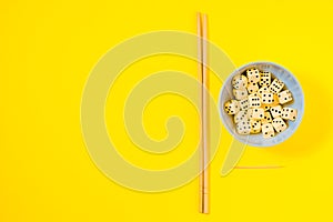 Dice in white bowl with chopsticks on yellow background