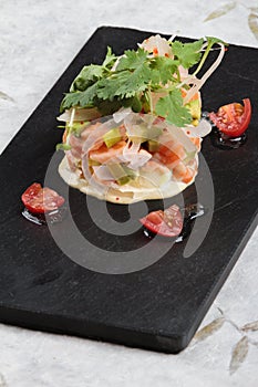 Diced salmon salad with avocado, tomato, onion, chilli, and coriander served in black rectangle stone plate on washi.