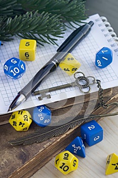 Dices for rpg, dnd, tabletop, or board games, pen, notebook, old decorated key, old books on a wooden surface.