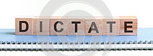 DICTATE - a word made of wooden blocks with black letters, a row of blocks is located on a blue Notepad