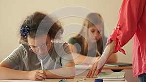 Dictation, final exam, schoolgirls write test. Children in the classroom are sitting at their desks. The teacher walks