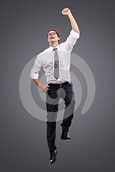 Did it. a happy young business man jumping in the air in celebration in front of a gray background.