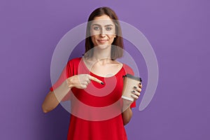 Did you drink your coffee today. Satisfied young pretty brunette girl in red t-shirt pointes to disposable cup with drink. Coffee