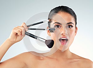 Did you hear about the best kept beauty secret. Studio shot of a beautiful young woman holding makeup brushes against a