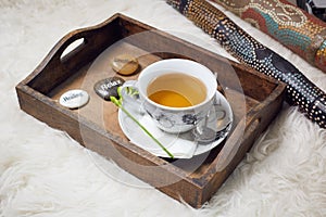 A didgeridoo and a wooden tablet with a filled teacup on it. Decorated with a flower and three labeled pebbles, Healing, Relax,