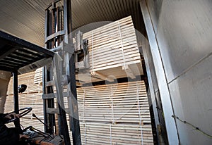 A diesel forklift loads freshly sawn pine logs, girders, bars, beams, bars, boards into a drying chamber. Industrial technology of