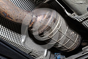 A diesel particulate filter in the exhaust system in a car on a lift in a car workshop, seen from below.