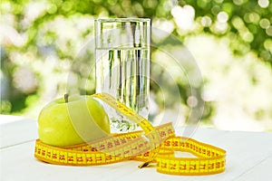 Diet. A apple with water and measuring tape on a white wooden table on green natural background. Health care concept