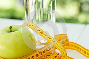 Diet. A apple with water and measuring tape on a white wooden table on green natural background. Health care concept