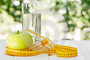 Diet. A apple with water and measuring tape on a white wooden table on green natural background. Health care concept. Healthy