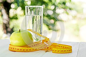Diet. A apple with water and measuring tape on a white wooden table on green natural background. Health care concept. Healthy