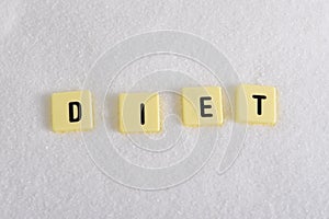 Diet block letters in crossword over sugar pile isolated on sweet grainy white sugar texture in dieting and healthy nutrition