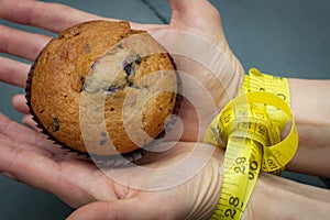 Diet, bondage and delayed gratification concept with woman hand reaching for a muffin while her hands are tied together with