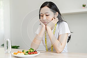Diet in bored face, unhappy beautiful asian young woman on dieting, looking at salad plate on table, dislike or tired with eat