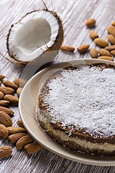 Diet cake with cocoa and coconut on a beige plate on a white wooden table against the background of almonds and broken coconut
