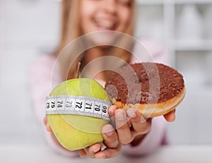 Diet choices concept with apple and doughnut in hands of smiling girl