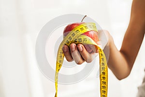 Diet concept. Apple with measure tape in female hand