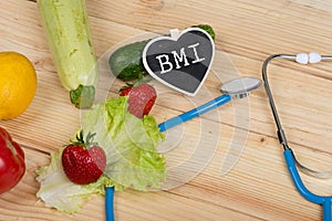 diet concept - Blackboard in shape of heart with text BMI Body mass index, stethoscope, vegetables, fruits and berries