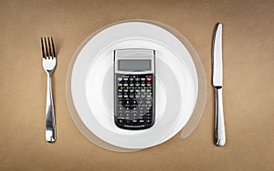 Diet concept with calculator on empty plate with fork and knife isolated on brown recycled paper background