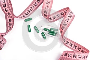 Diet concept. Diet pills, green capsules with pink measuring tape on a white background
