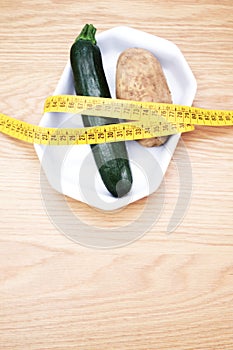 Diet concept - fresh organic zucchini and potato rapped in a measuring tape on a wooden table