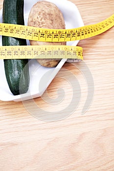 Diet concept - fresh organic zucchini and potato rapped in a measuring tape on a wooden table