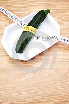 Diet concept - fresh zucchini in a white bowl rapped in a measuring tape on a wooden table