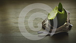 Diet concept. Green apple bite with measuring tape on wooden background with copy space