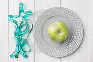 Diet concept. Green Apple on a plate and tape centimeter on a white table