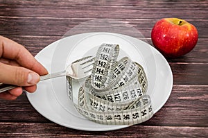 Diet concept. Measuring tape in a white plate on a wooden table and an apple.