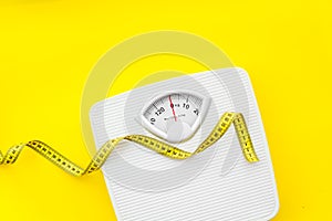 Diet concept with scale and measuring tape for weight loss on yellow background top view