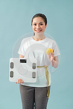 Diet and fitness concept - beautiful sporty woman with scale, yellow apple and measuring tape