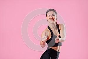 Diet and fitness concept - beautiful sporty woman showing thumbs up and her abs. Hand in the foreground shows a finger up gesture