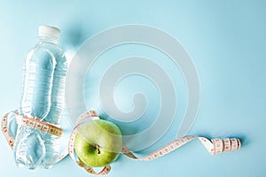 Diet flat lay one meter ribbon and green apple and a bottle of water. blue background with copy space. health sport concept