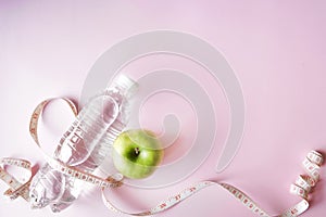 Diet flat lay one meter ribbon and green apple and a bottle of water. pink background with copy space. health concept