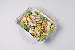 Diet fresh meat salad with a lot of greens, grilled chicken, feta on white background. Healthy low-calorie lunch in foil